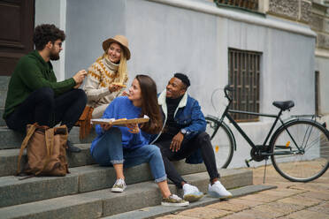 Eine Gruppe fröhlicher junger Leute, die draußen in der Stadt Pizza essen. Coronavirus-Konzept. - HPIF14106