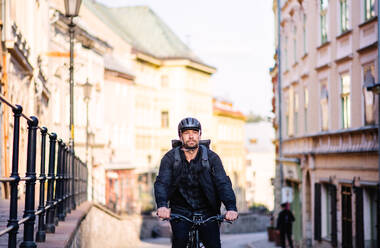 Front view of delivery man courier with bicycle cycling in small town. - HPIF14119