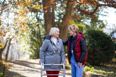 Ältere Frau mit Rollator und Pflegerin oder medizinischem Personal bei einem Spaziergang im Park, Coronavirus-Konzept. - HPIF14125