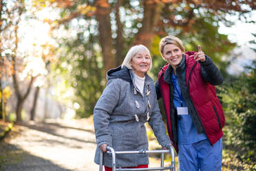 Ältere Frau mit Rollator und Pflegerin oder medizinischem Personal bei einem Spaziergang im Park, Coronavirus-Konzept. - HPIF14127