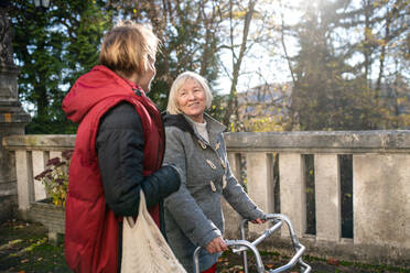 Ältere Frau mit Gehhilfe und Betreuerin oder Pflegekraft im Freien bei einem Spaziergang im Park. - HPIF14142