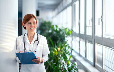 Porträt einer Ärztin mit Klemmbrett im Krankenhaus stehend, Kopierraum. - HPIF14232