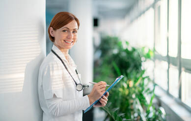 Portrait of woman doctor with clipboard standing in hospital. Copy space. - HPIF14233