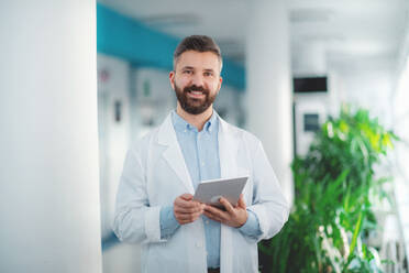 Portrait of man doctor standing in hospital, using tablet. Copy space. - HPIF14235