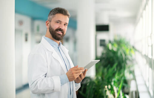 Porträt eines Arztes, der im Krankenhaus steht und ein Tablet benutzt, Kopierraum. - HPIF14236