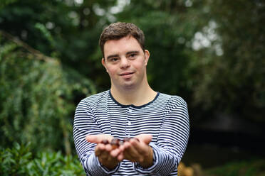 Portrait of down syndrome adult man standing outdoors at green background, holding nuts in hands. - HPIF14243