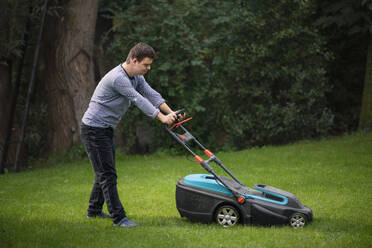 Portrait of down syndrome adult man mowing lawn outdoors in backyard, helping with housework concept. - HPIF14248