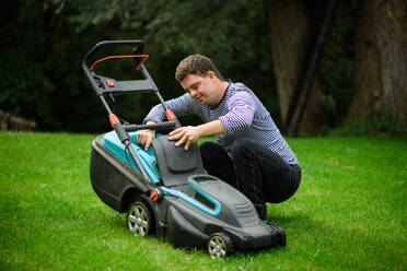 Portrait of down syndrome adult man mowing lawn outdoors in backyard, helping with housework concept. - HPIF14249