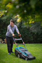 Portrait of down syndrome adult man mowing lawn outdoors in backyard, helping with housework concept. - HPIF14250