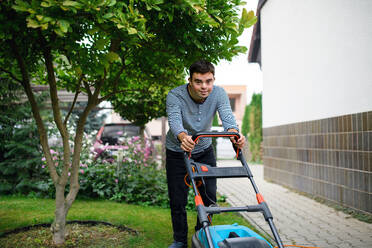 Portrait of down syndrome adult man mowing lawn outdoors in backyard, helping with housework concept. - HPIF14252