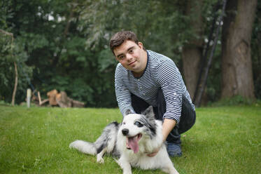 Portrait of cheerful down syndrome adult man playing with dog pet outdoors in backyard. - HPIF14260