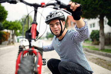 Porträt eines erwachsenen Mannes mit Down-Syndrom, der mit Fahrrad und Helm im Freien auf der Straße steht. - HPIF14271