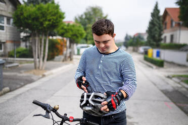 Porträt eines erwachsenen Mannes mit Down-Syndrom, der mit Fahrrad und Helm im Freien auf der Straße steht. - HPIF14272
