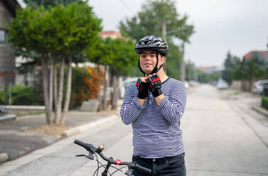 Porträt eines erwachsenen Mannes mit Down-Syndrom und Fahrrad, der im Freien auf der Straße steht und in die Kamera schaut. - HPIF14273