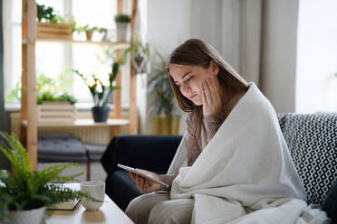 Besorgte junge Frau, eingewickelt in eine Decke, die zu Hause ein Tablet benutzt, Konzept des Coronavirus. - HPIF14323