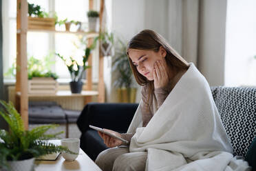 Worried young woman wrapped in blanket using tablet at home, coronavirus concept. - HPIF14323