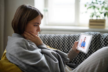 Eine kranke junge Frau führt ein Videogespräch mit einem Arzt auf einem Tablet zu Hause, Konzept der Online-Konsultation. - HPIF14329