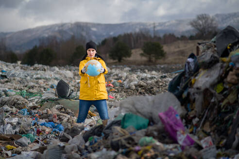 Frontansicht einer Frau mit Globus, die auf einer Mülldeponie steht, Umweltkonzept, Raum kopieren. - HPIF14379