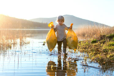 Small child collecting rubbish outdoors by lake in nature, plogging concept. - HPIF14412