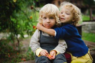 Glückliche kleine Kinder sitzen im Freien im Garten, nachhaltiger Lebensstil Konzept. - HPIF14440