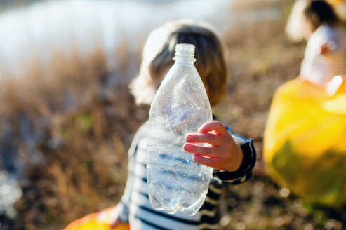 Unkenntlich kleines Kind mit Plastikflasche sammelt Müll draußen in der Natur, plogging Konzept. - HPIF14450