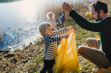 Älterer Vater mit kleinen Kindern, die draußen in der Natur Müll sammeln, Plogging-Konzept. - HPIF14452