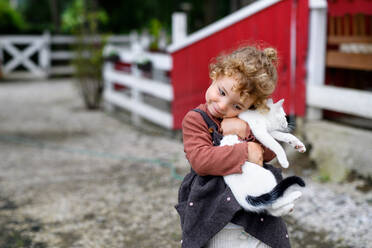 Portrait of small girl with cat standing on farm, playing. - HPIF14493
