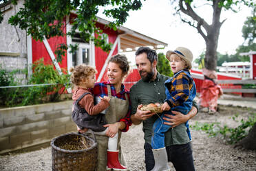 Portrait of happy family with small children standing on farm, holding basket with eggs. - HPIF14502