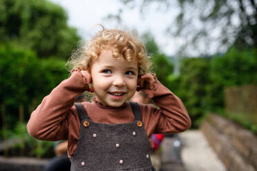 Porträt eines niedlichen kleinen Mädchens, das auf einem Bauernhof steht und Kirschenohrringe hält. - HPIF14528