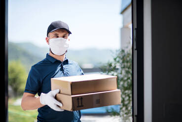 Front view of courier with face mask delivering parcel, corona virus and quarantine concept. - HPIF14548