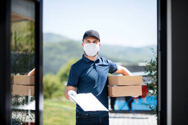 Front view of courier with face mask delivering parcel, corona virus and quarantine concept. - HPIF14549