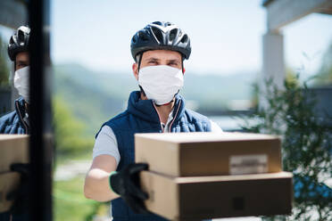 Front view of courier with face mask delivering parcel, corona virus and quarantine concept. - HPIF14550