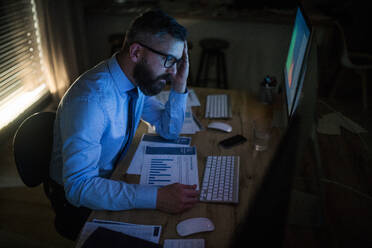 Frustrierter und besorgter Geschäftsmann mit Computer am Schreibtisch sitzend, spät arbeitend, Konzept der Finanzkrise. - HPIF14563