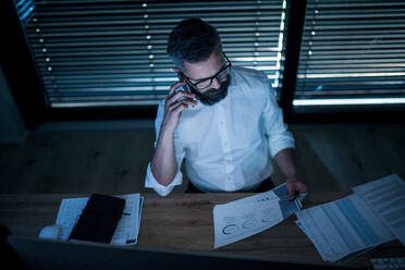 Top view of mature businessman with smartphone sitting at desk, working late. Financial crisis concept. - HPIF14583