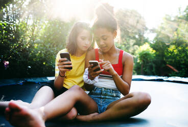 Front view of cheerful young teenager girls friends outdoors in garden, using smartphone. - HPIF14600