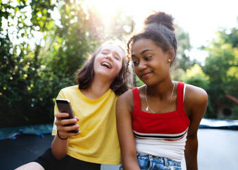 Vorderansicht von fröhlichen jungen Teenager-Mädchen, die sich im Garten aufhalten und ein Smartphone benutzen. - HPIF14601