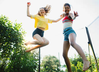 Low angle view of cheerful young teenager girls friends outdoors in garden, jumping on trampoline. - HPIF14603
