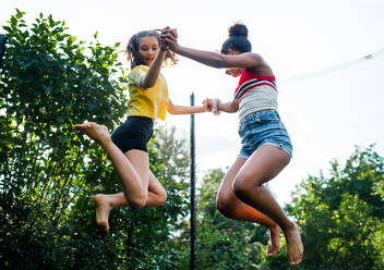 Niedriger Winkel Blick auf fröhliche junge Teenager-Mädchen Freunde im Freien im Garten, Springen auf Trampolin. - HPIF14637