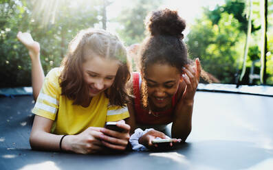 Vorderansicht von fröhlichen jungen Teenager-Mädchen, die sich im Garten aufhalten und ein Smartphone benutzen. - HPIF14641