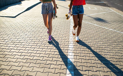 Unrecognizable teenager girls friends with skateboards walking outdoors in city, midsection. - HPIF14647