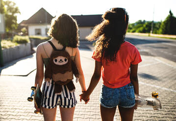 Rückansicht von Teenager-Mädchen Freunde mit Skateboards zu Fuß im Freien in der Stadt. - HPIF14649