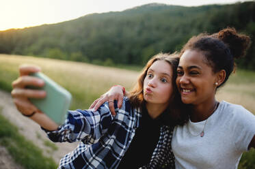 Lächelnde Teenager-Mädchen halten einen lustigen Moment in der Natur mit einem Selfie mit ihren Smartphones fest - HPIF14661