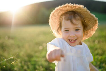 Porträt eines kleinen Mädchens, das im Sommer auf einer Wiese steht und in die Kamera schaut. - HPIF14682