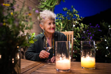 Porträt einer glücklichen älteren Frau am Abend auf der Terrasse, die Wein trinkt. - HPIF14726