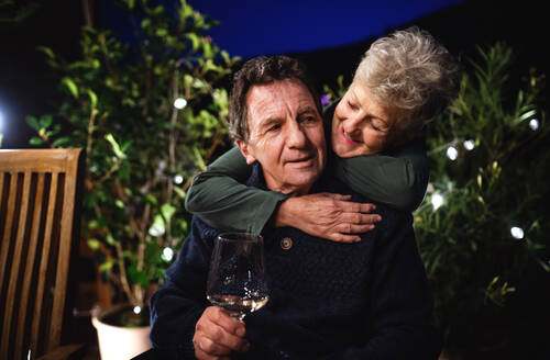 Porträt eines älteren Paares bei Wein auf der Terrasse, das sich umarmt. - HPIF14727