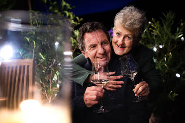 Porträt eines älteren Paares mit Wein am Abend auf der Terrasse, das in die Kamera schaut. - HPIF14728