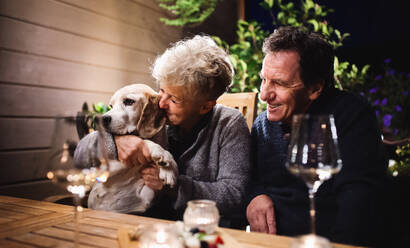 Porträt eines älteren Paares mit Hund am Abend auf der Terrasse, Wein trinkend. - HPIF14731