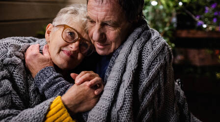 Close-up portrait of senior couple sitting in the evening on terrace, hugging. - HPIF14758