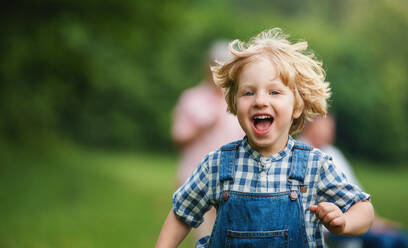 Porträt eines kleinen Jungen mit unkenntlichen Großeltern bei einem Spaziergang auf einer Wiese in der Natur, beim Laufen. - HPIF14769