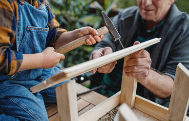 Midsection of unrecognizable small boy with senior grandfather constructing birdhouse, diy project. - HPIF14797